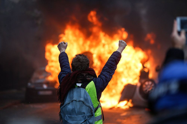 Một người biểu tình đứng trước xe ô tô bị đốt tại Paris hôm 1 12